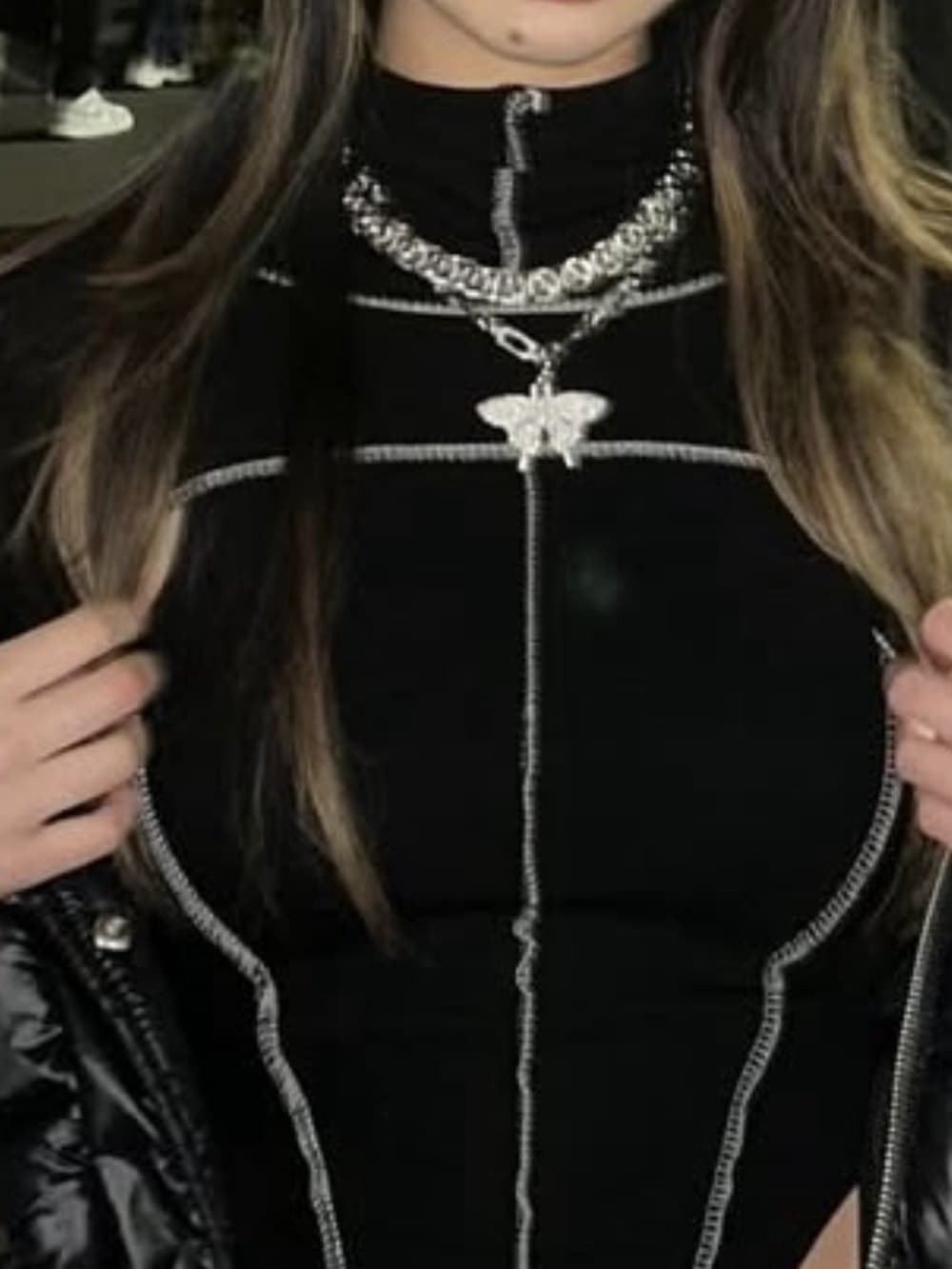 Close-up of a black going-out top layered with a chain necklace and butterfly pendant