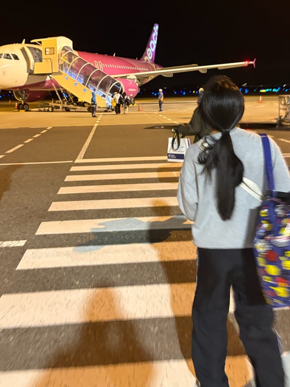 Boarding a pink Peach airlines plane across the tarmac at night