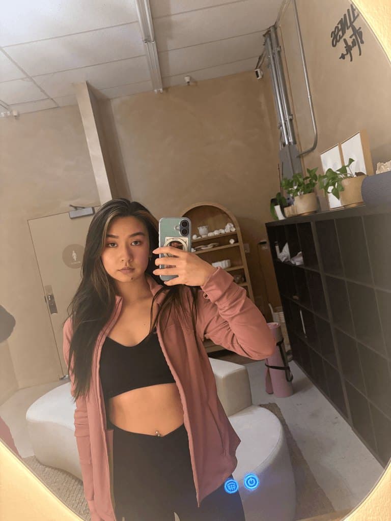 Helen in a gym mirror selfie wearing a pink zip jacket over a black set